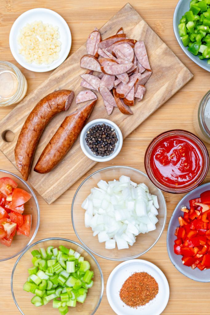 Overhead mise en place for paleo jambalaya with sliced sausage, vibrant fresh vegetables, and whole, dietary-friendly ingredients